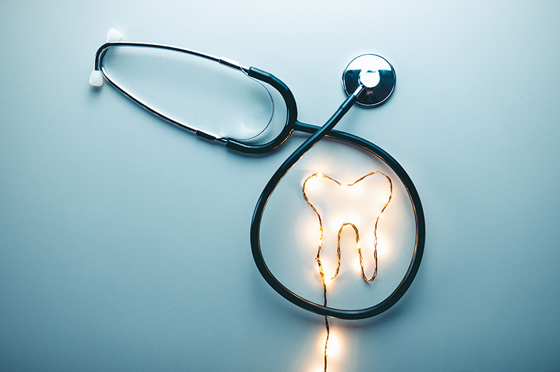 Grafika przedstawiająca zęba jako pasek led z ciepłym światłem. W okoł niego owinięty jest stetoskop.