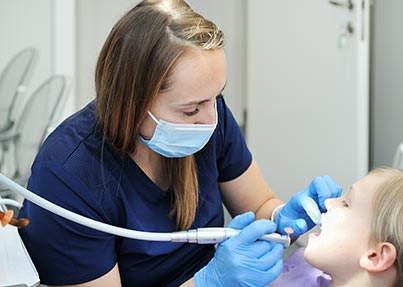Stomatolog wykonuje zabieg plombowania zęba u małoletniego pacjenta