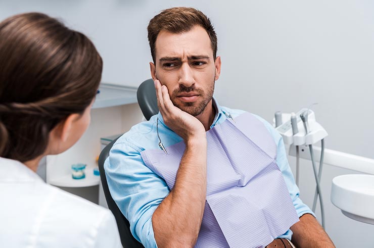 Pacjent trzymający się za twarz słucha rad Dentysty