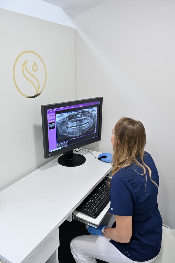 Dentystka Joanna siedzi przed komputerem, na którym widnieje rentgen szczęki