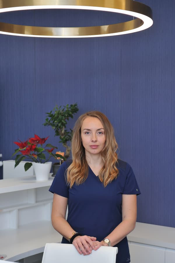 Dentystka Joanna Szewczyk - Niedźwiecka stoi w recepcji i opiera ręcę o białe krzesło