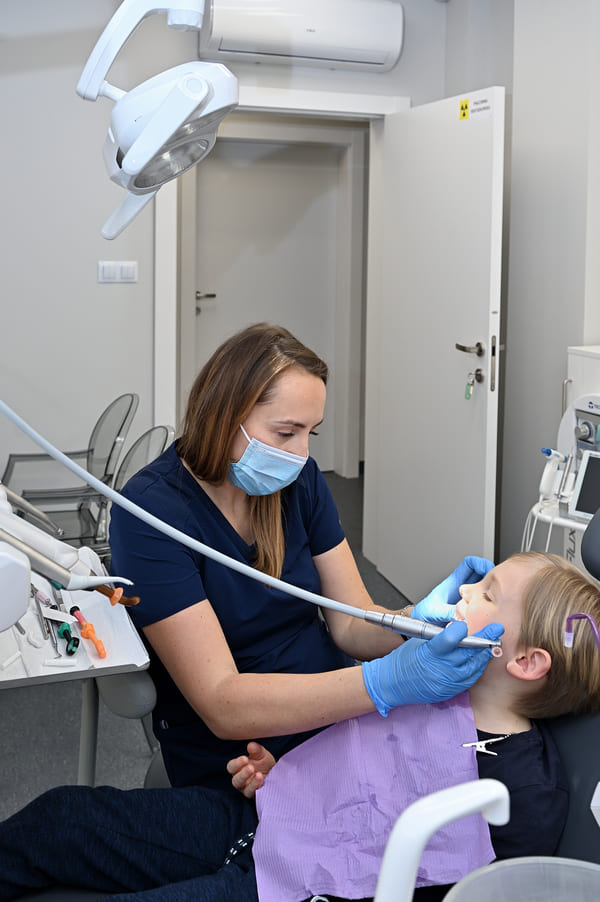 Dentystka Joanna wykonująca zabieg dentystyczny u nastolatka - zdjęcie z boku