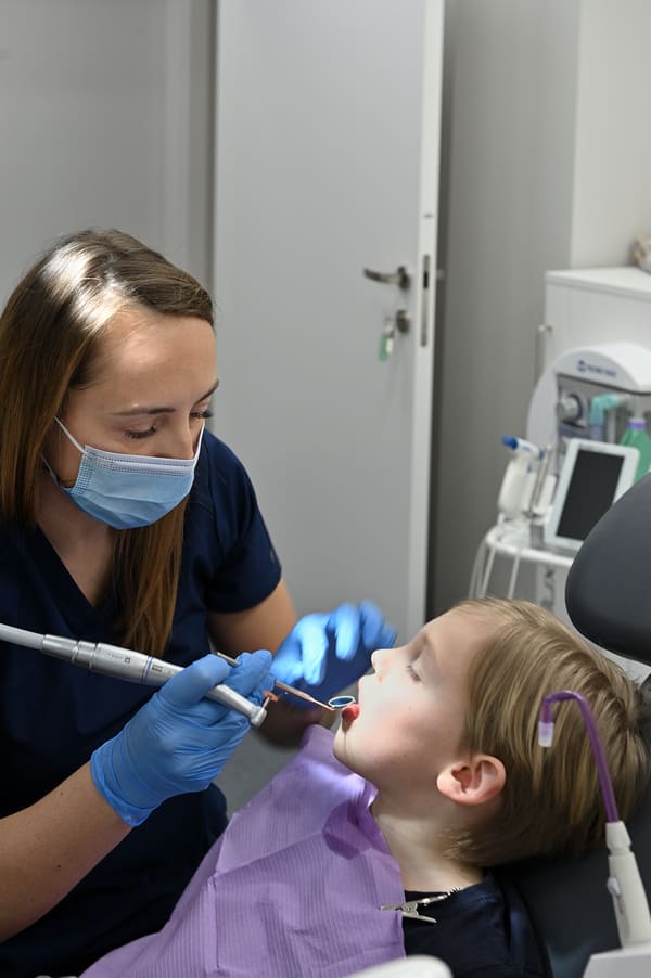 Dentystka Joanna wykonująca zabieg dentystyczny u chłopca - zdjęcie z bocznej perspektywy